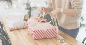Photo of a woman at a table wrapping a christmas present with wrapping paper and ribbons
